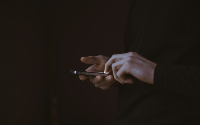 Silhouette of a person looking at a glowing smartphone screen in the dark