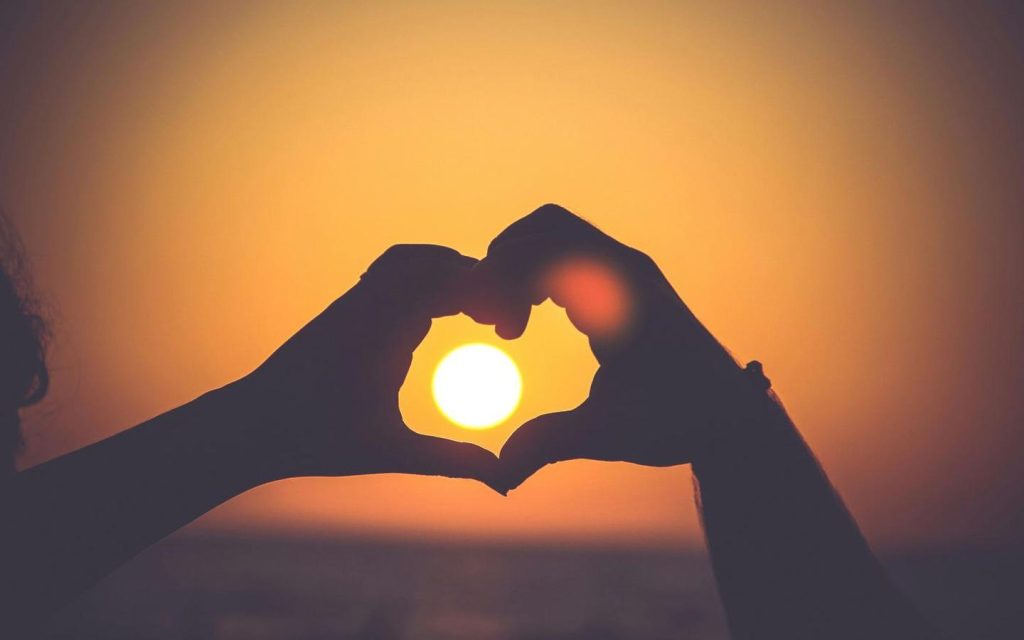Hands forming a heart around the setting sun