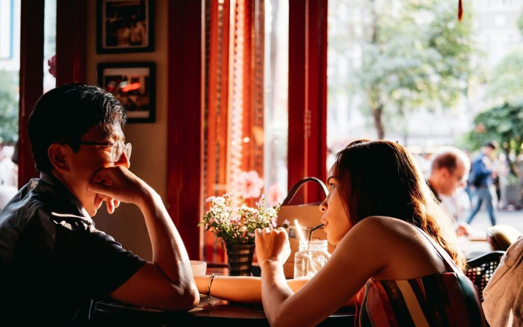 Couple laughing across a table in a sunlit café