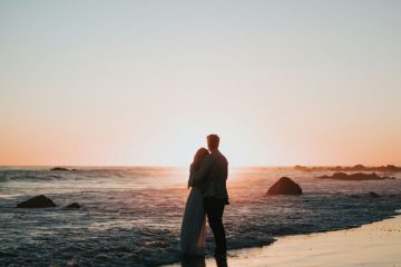 Couple embracing at the water’s edge at sunset