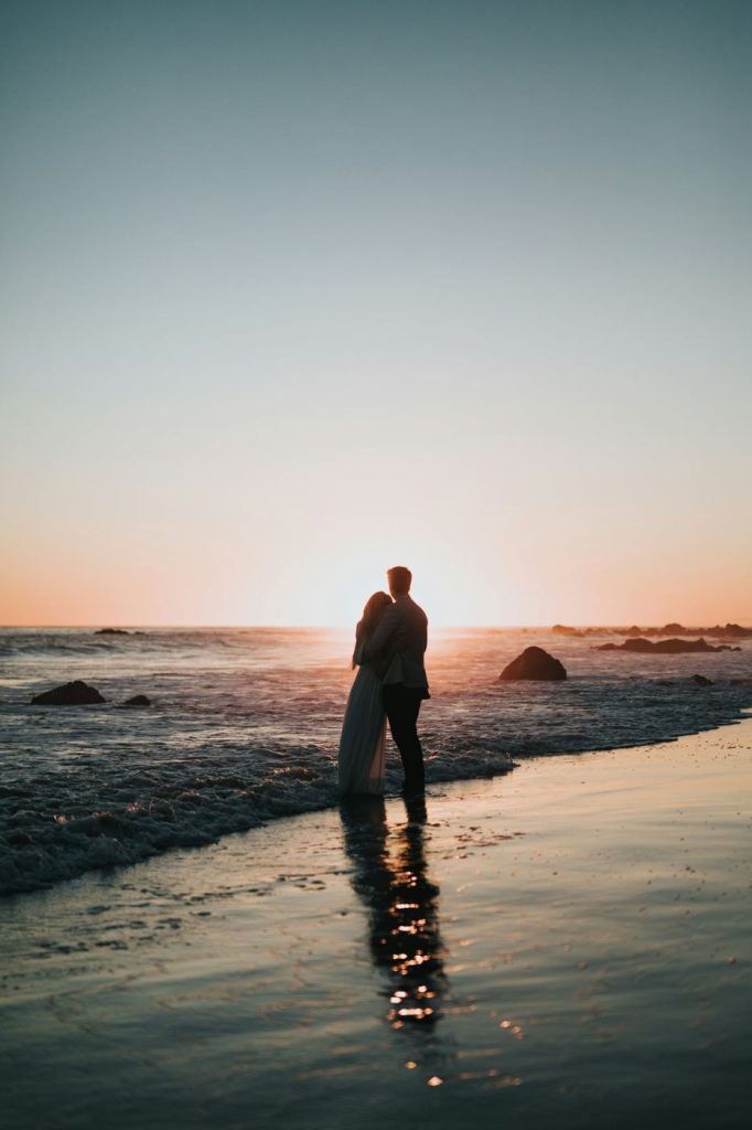 Couple embracing at the water’s edge at sunset