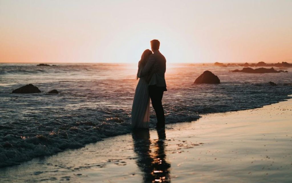 Couple embracing at the water’s edge at sunset