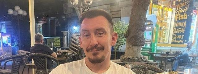 Dimitry Perepelin in a white T-shirt sitting at a wicker table in a café