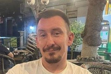 Дмитрий Перепелин в белой футболке сидит за плетеным столиком в кафе