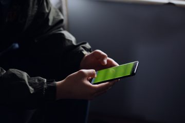 A hand holding a smartphone with a cracked screen in low light