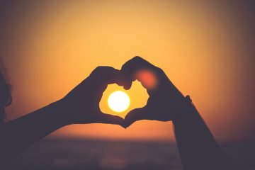 Silhouetted hands forming a heart around the setting sun