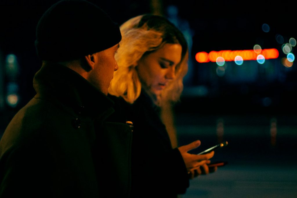 Мужчина и женщина в полумраке вместе смотрят на экран смартфона
