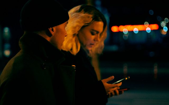 Мужчина и женщина в полумраке вместе смотрят на экран смартфона