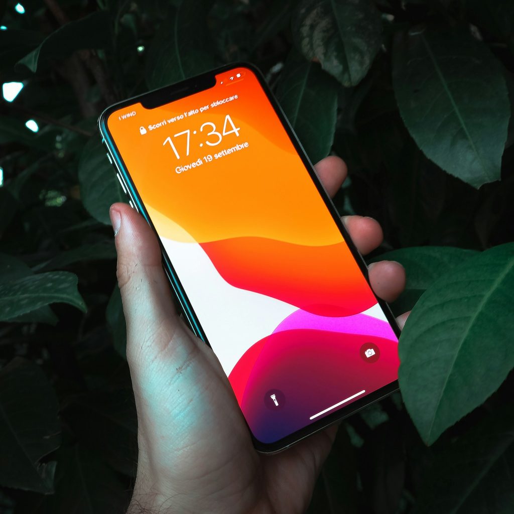 Рука держит смартфон с включённым экраном на тёмном фоне