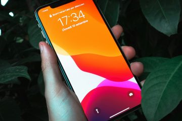 Рука держит смартфон с включённым экраном на тёмном фоне