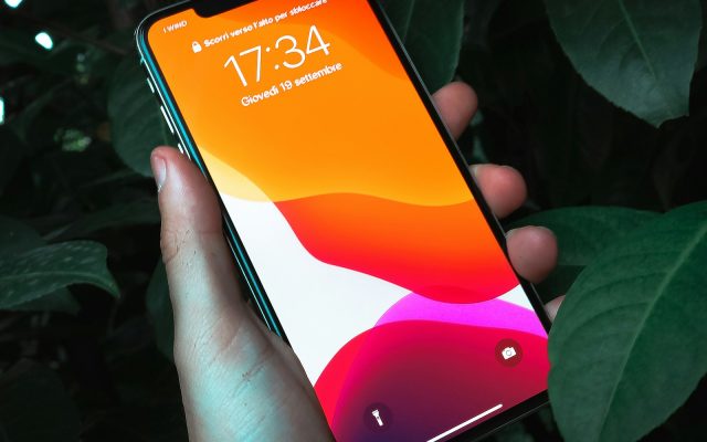 Рука держит смартфон с включённым экраном на тёмном фоне